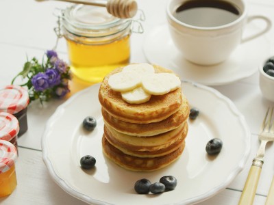 Breakfast 2 2 ppeeb5gg6lti9ognwwocqvya1vl8e08sbf1nw3pyuw About Homey From above view of pancakes served in white plate decorated with slices of banana and blueberries with cup of coffee and honey placed near on white background.